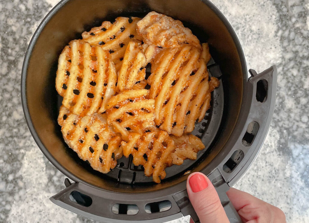 Frozen waffle fries in air fryer basket. 