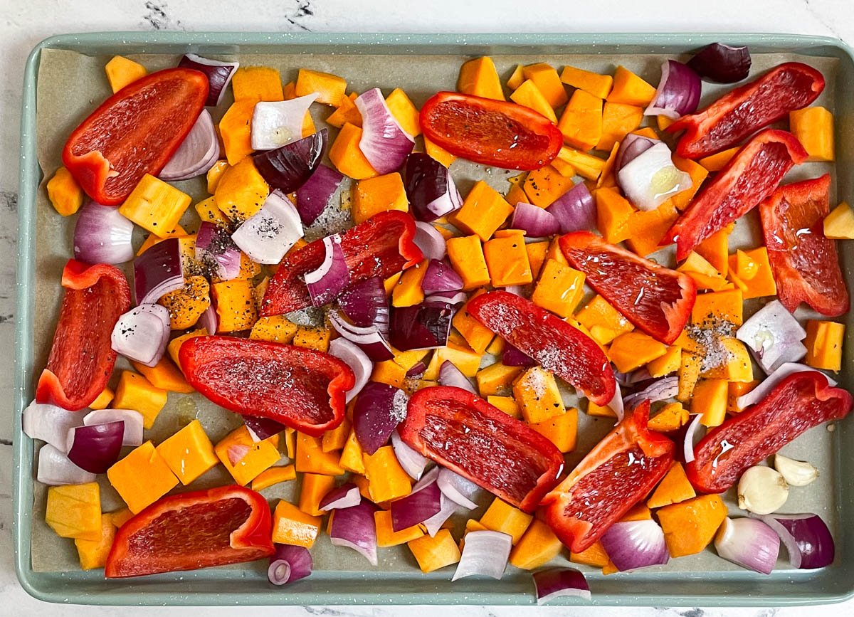 Butternut squash, red pepper slices and onions on a baking sheet.

