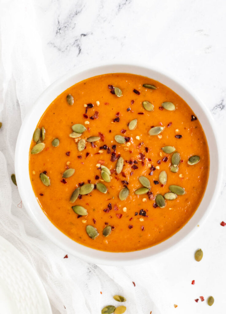 Butternut squash soup in white bowl topped with red pepper flakes and pumpkin seeds. 