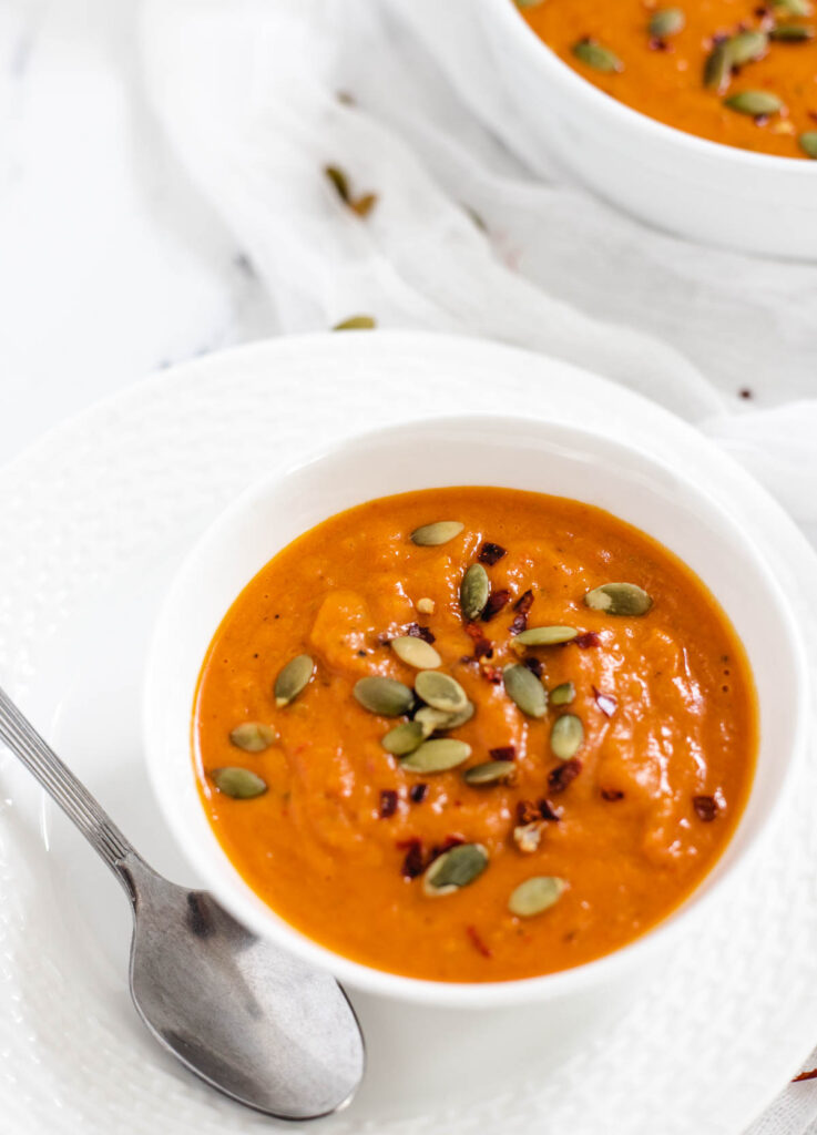 Creamy roasted red pepper soup in white bowl spoon. 