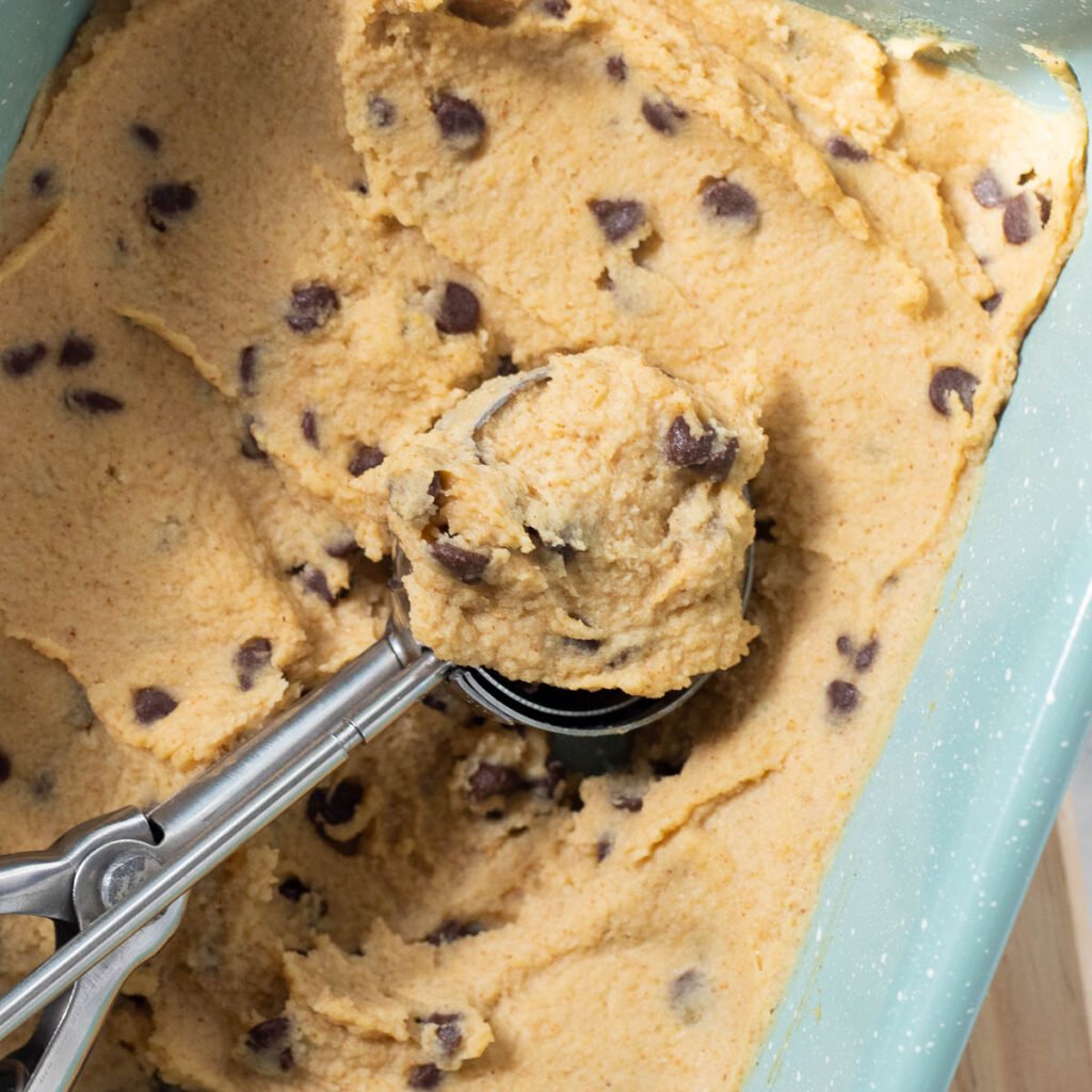 Chickpea cookie dough in baking sheet with cookie scoop.