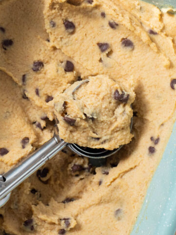 Chickpea cookie dough in baking sheet with cookie scoop.