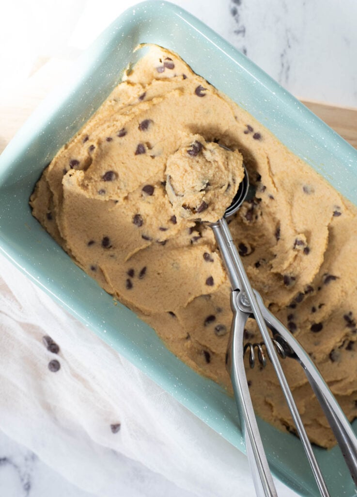 Edible cookie dough in baking pan with scoop of chickpea cookie dough. 
