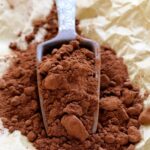 Cocoa powder in scoop on top of brown paper.