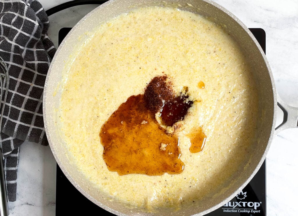 Adding maple syrup, nutmeg and salt to creamy cornmeal in pot. 