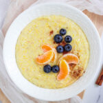 Cornmeal porridge in white bowl topped with blueberries and orange slices.