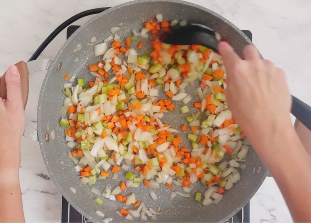 Stirring onions, celery, and carrots in pot. 