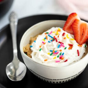 Vegan vanilla mug cake topped with whipped cream and sprinkles.
