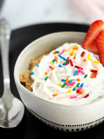 Vegan vanilla mug cake topped with whipped cream and sprinkles.