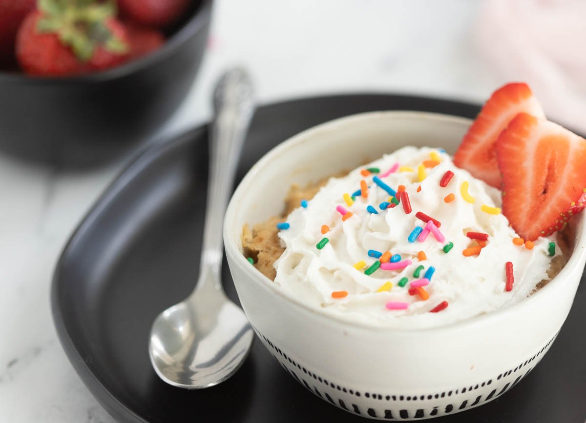 Small vanilla mug cake topped with whipped cream and sprinkles.