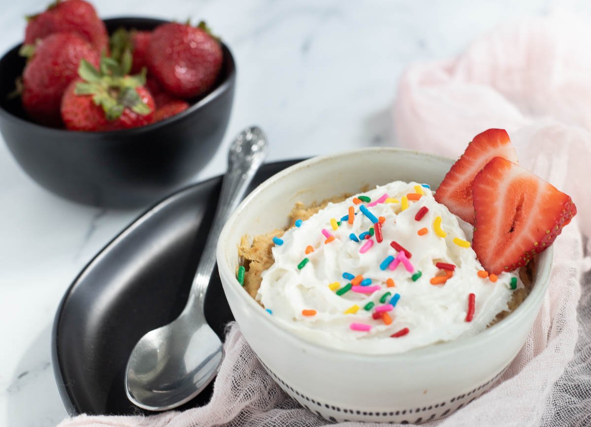 Vegan vanilla mug cake topped with coconut whipped cream, sprinkles, and strawberry slices. 