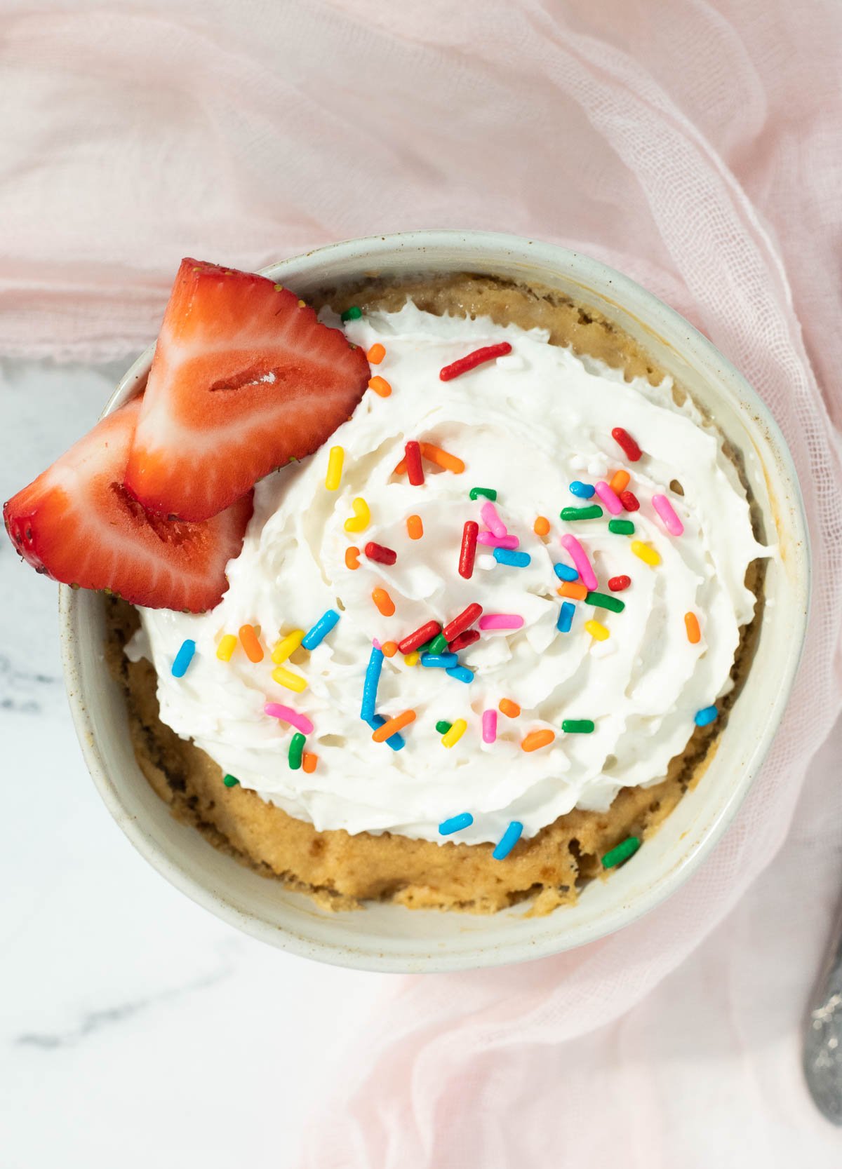 Overhead of mug cake topped with whipped cream and sprinkles.
