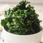 Air fryer kale chips piled high in white bowl.