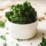 Air fryer kale chips piled high in white bowl.