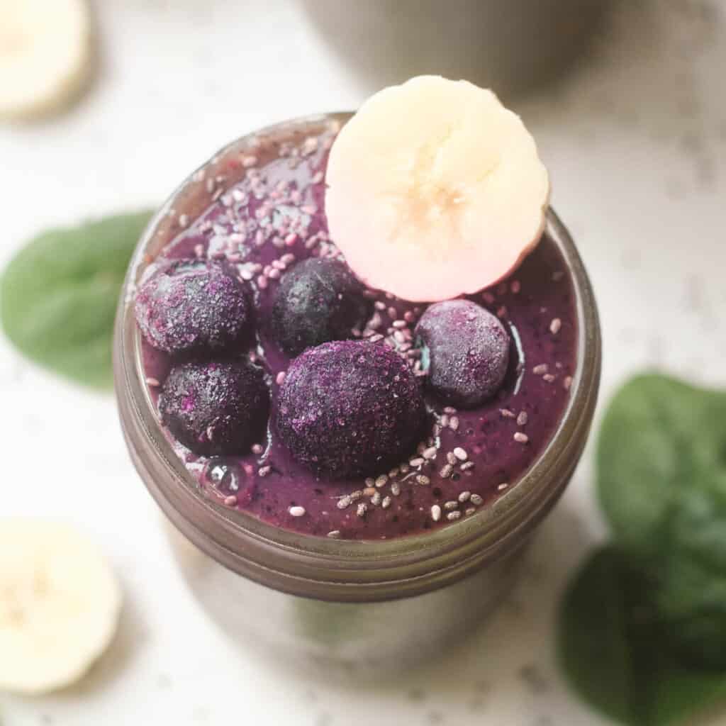 Blueberry smoothie topped with frozen blueberries and banana in a mason jar. 