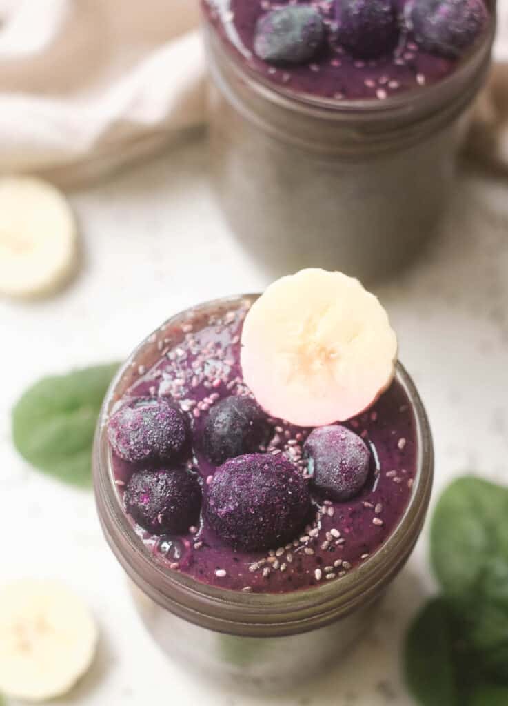 Spinach blueberry smoothie topped with frozen blueberries and banana in a mason jar. 