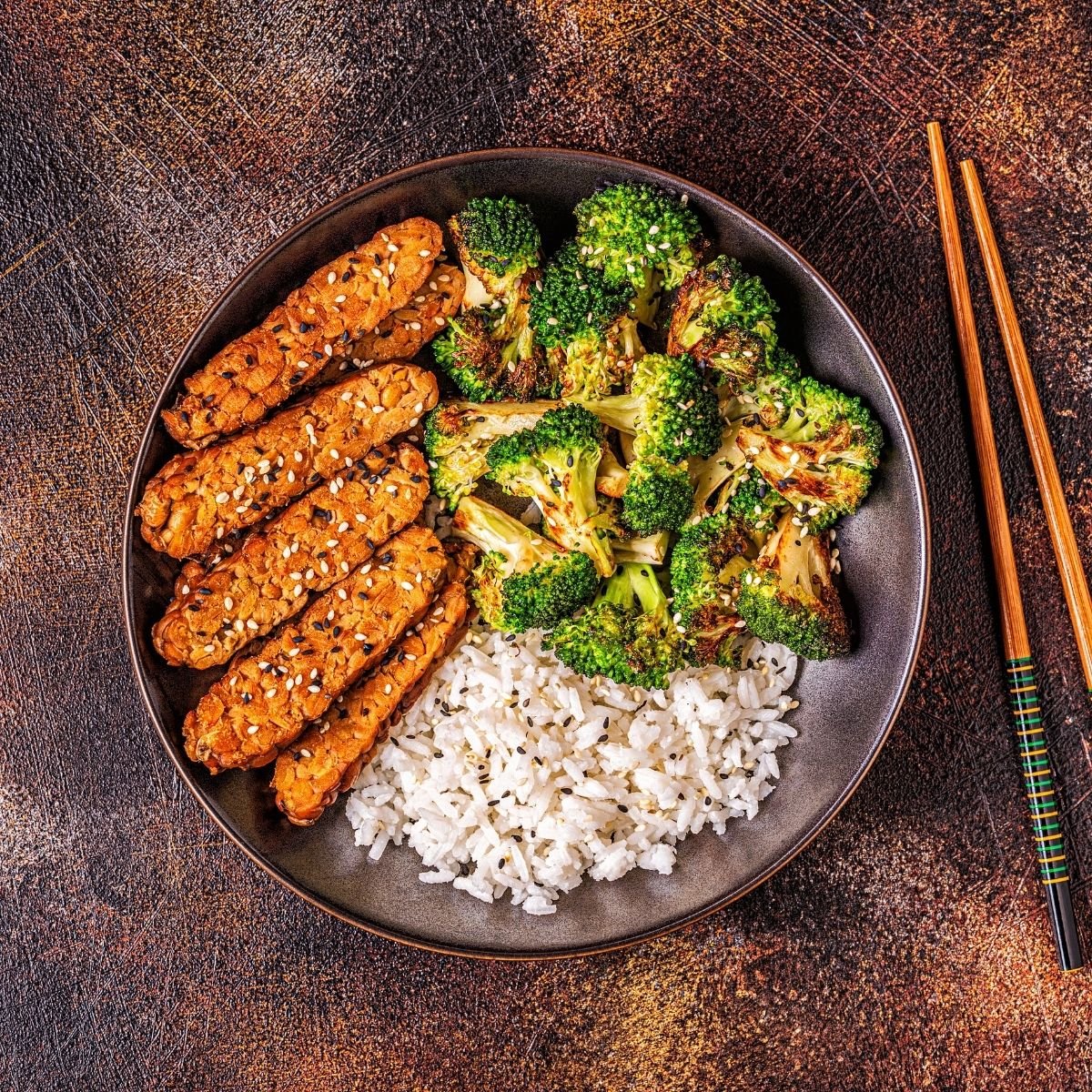 Sliced tempeh, broccoli, and rice in bowl served with chopsticks. 