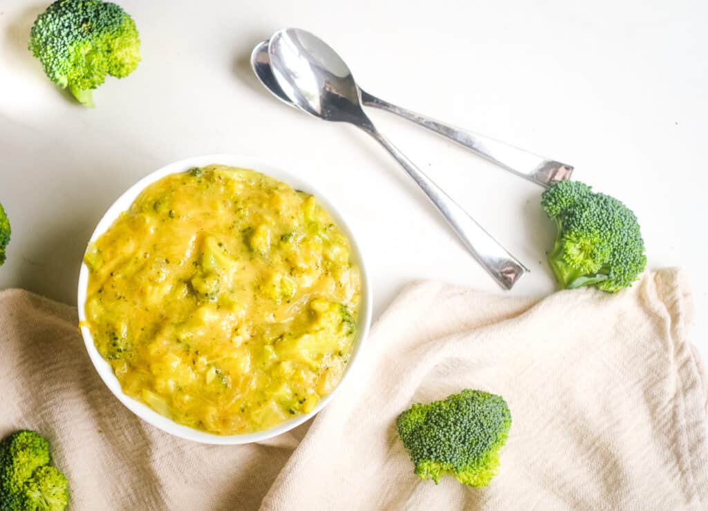 Bowl of broccoli cheddar soup with two spoons and broccoli florets. 