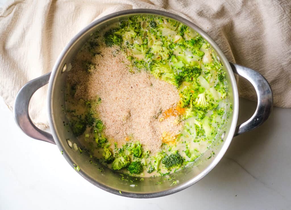 Nutritional yeast and spices added to pot of broccoli and broth. 