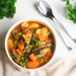 Vegan stew in white bowl with soup spoons.