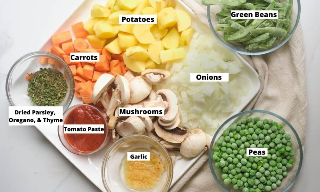 Ingredients for vegan stew: diced potatoes, diced onions, sliced mushrooms, diced carrots, dried herbs, tomato paste, garlic, frozen peas, and frozen green beans. 
