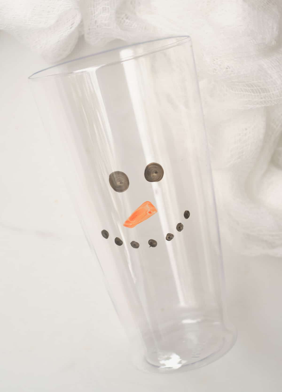Plastic cup with snowman face drawn on the front.