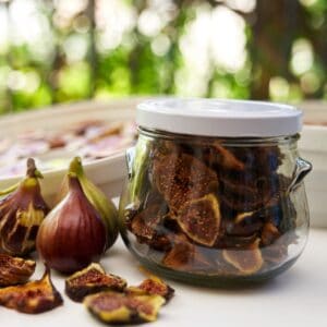 Dried figs in jar on table beside fresh figs and dried fig pieces.