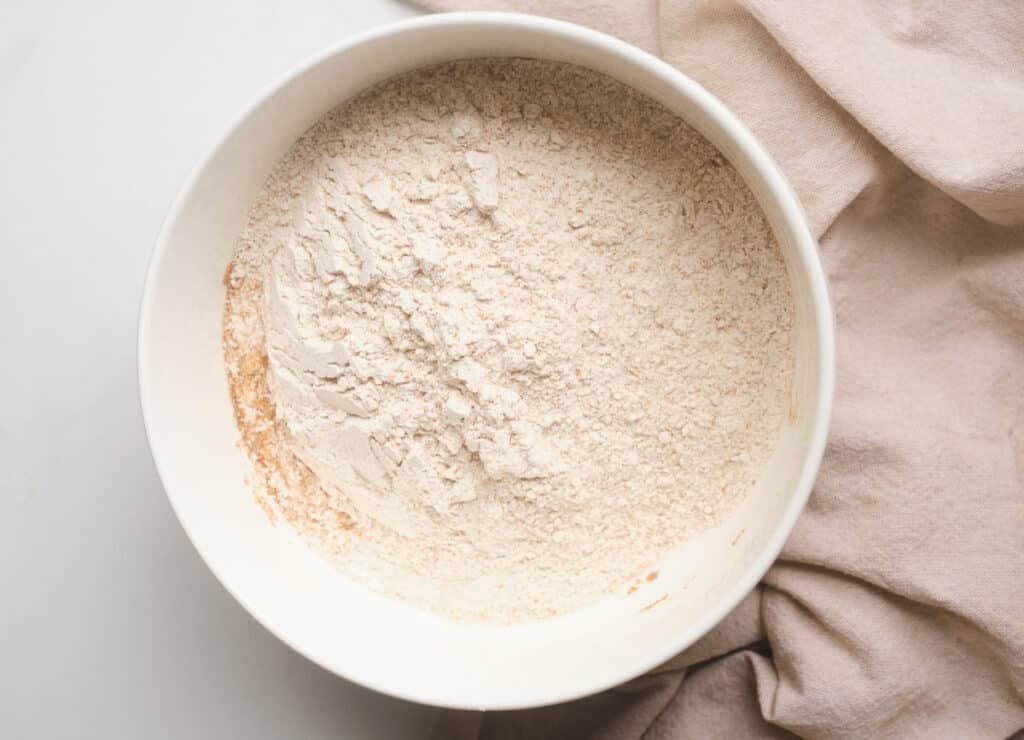 Flour, baking powder, baking soda, and spices whisked together in a white bowl. 