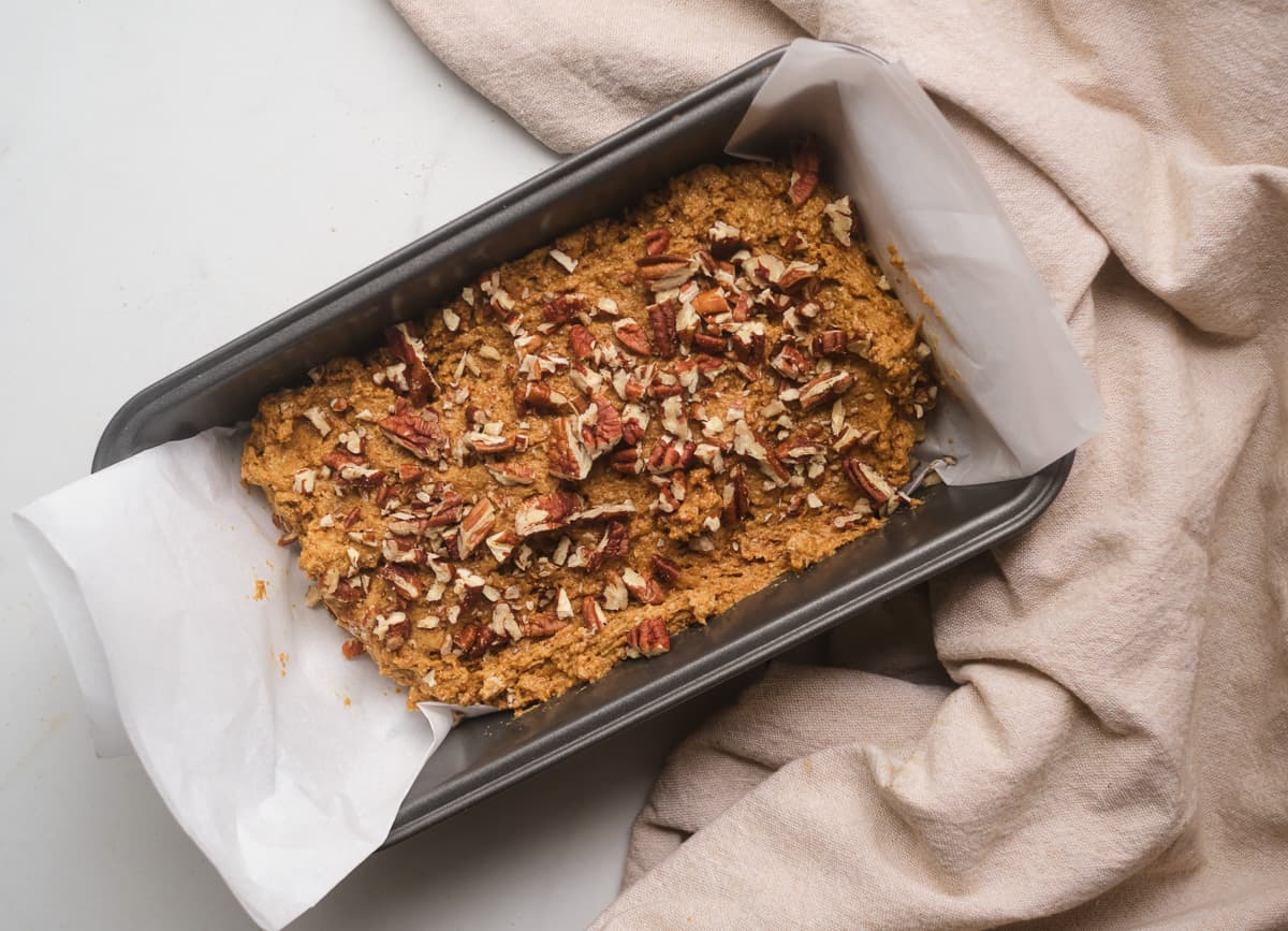 Gingerbread loaf batter in loaf pan, topped with pecans.