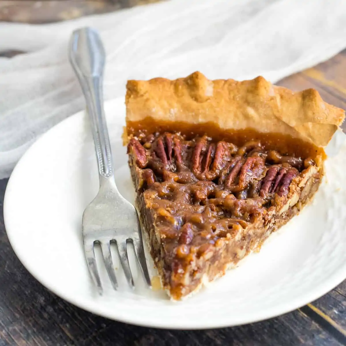 Slice of pecan pie on white plate with fork.