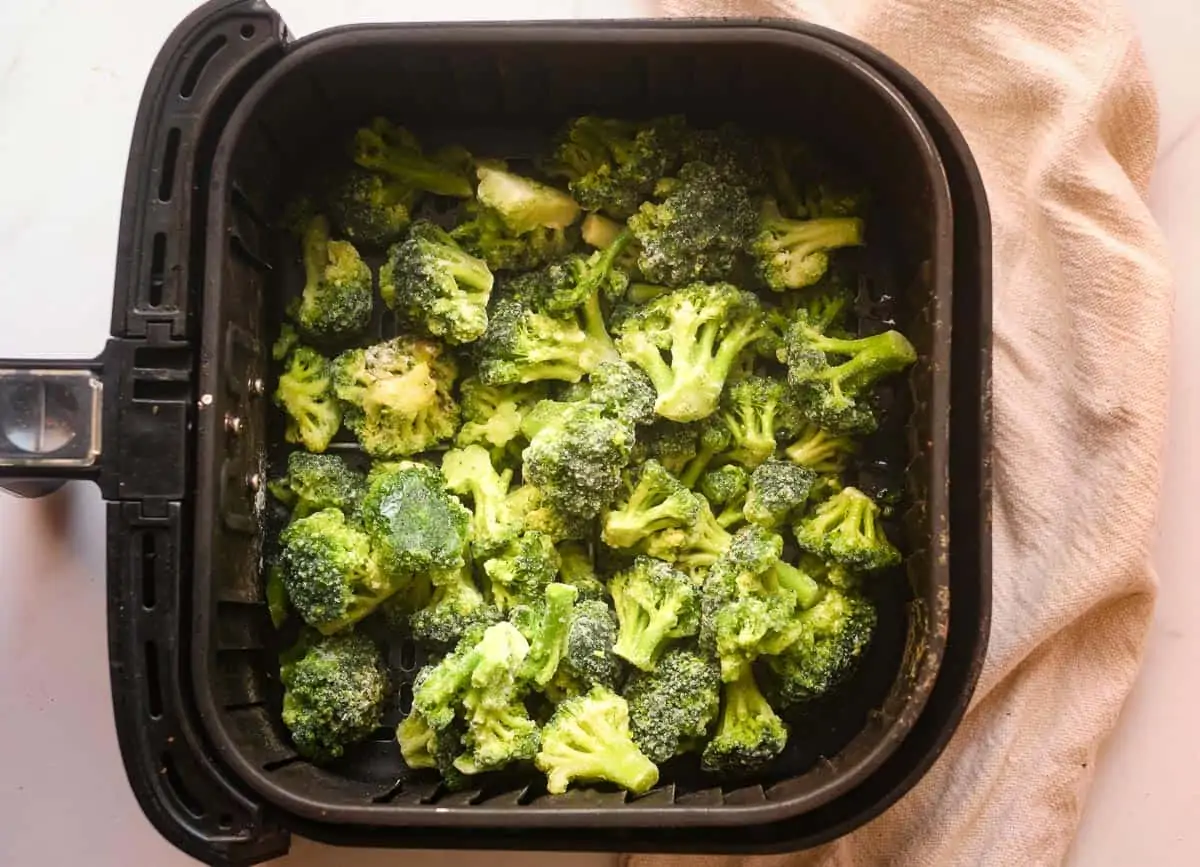 Frozen broccoli florets in an air fryer basket.
