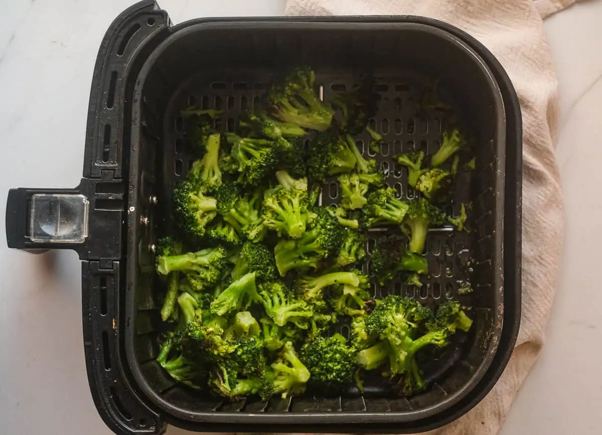 Cooked broccoli florets in an air fryer basket.
