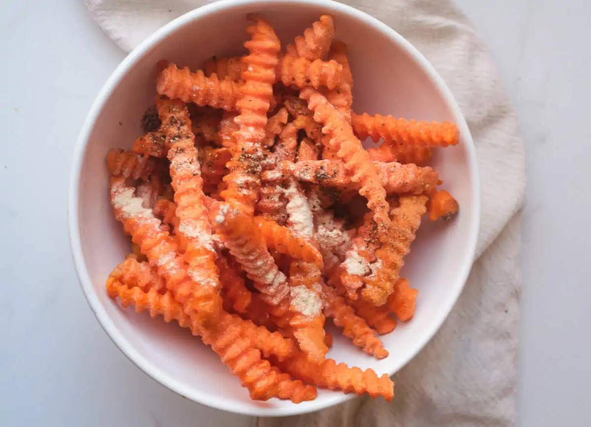 Crinkle sweet potato fries topped with spices in a white bowl.
