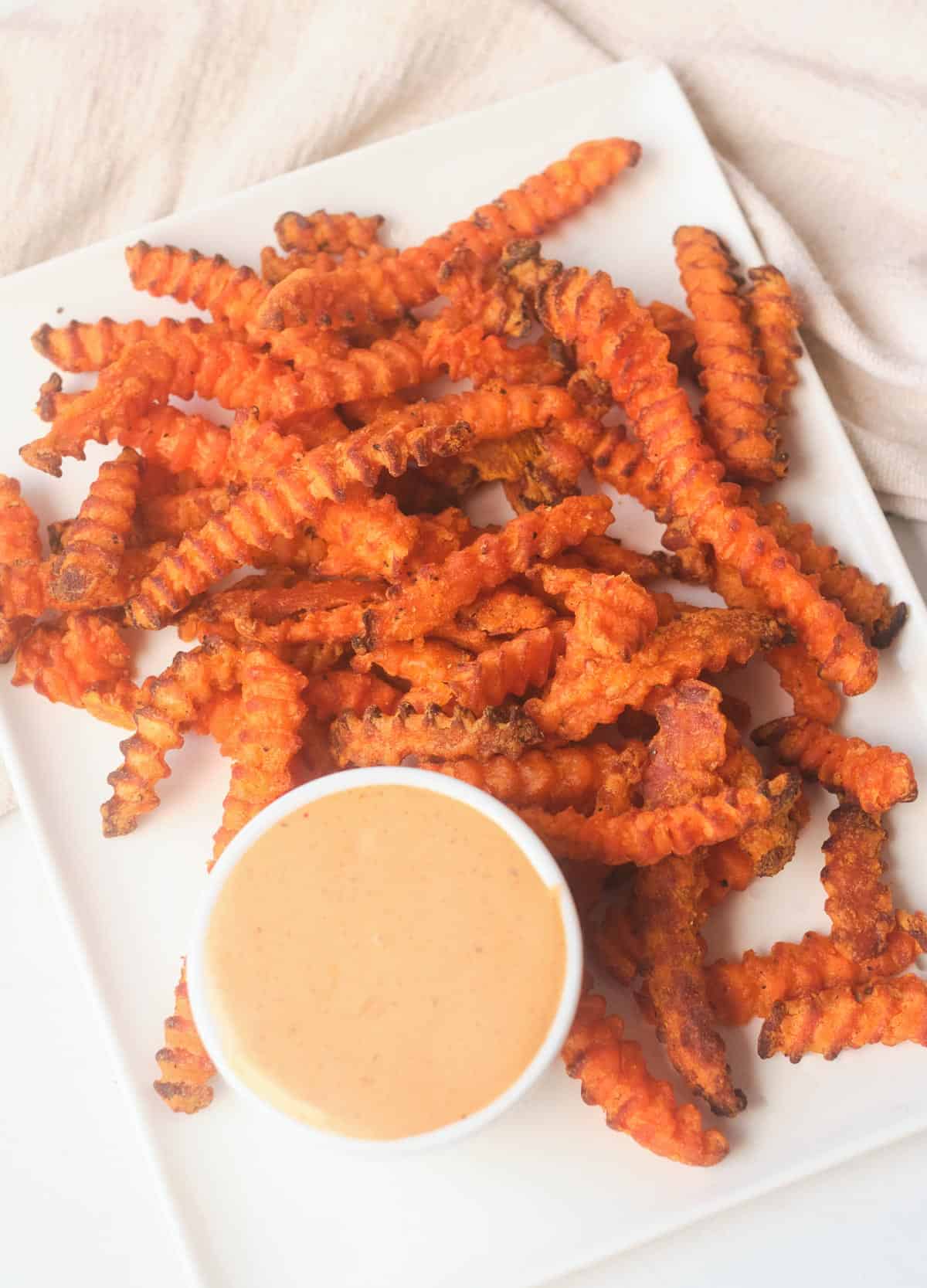 Cooked air fryer frozen sweet potato fries on a plate with dipping sauce. 