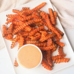 Cooked air fryer frozen sweet potato fries on plate with dipping sauce.