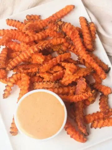 Cooked air fryer frozen sweet potato fries on plate with dipping sauce.