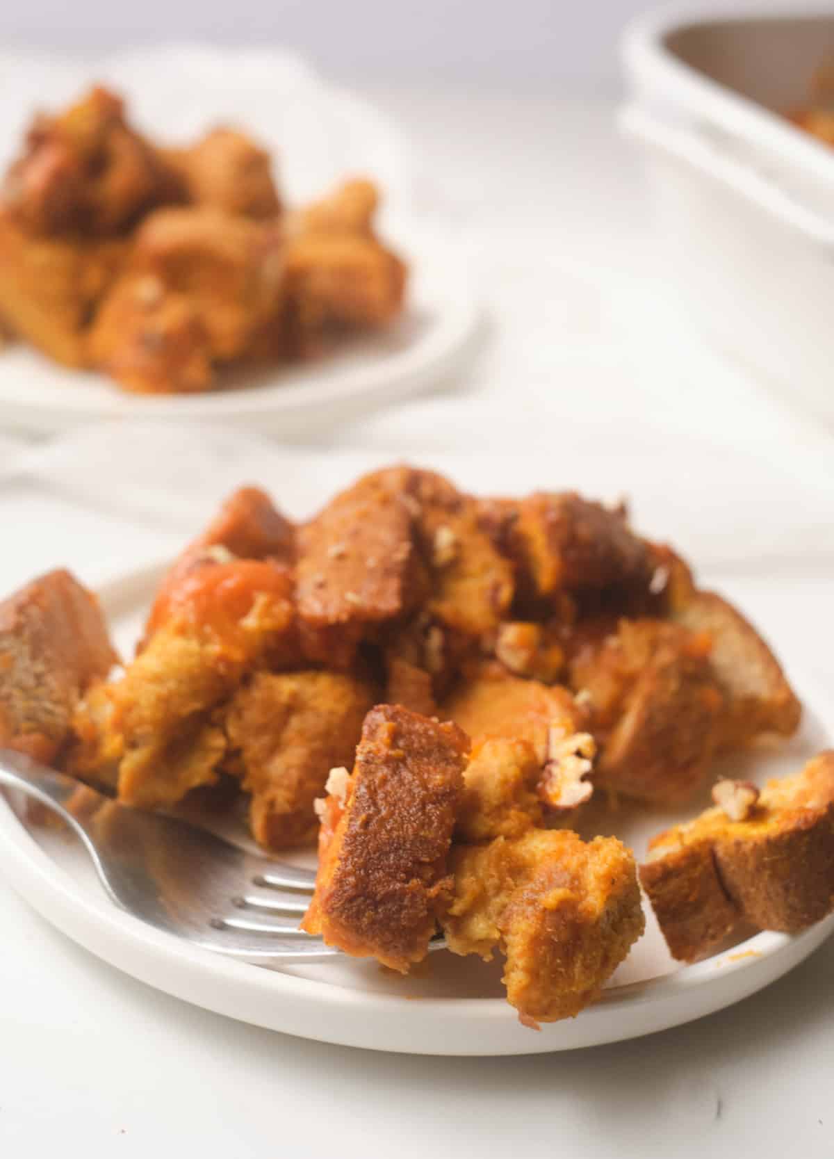 Serving of pumpkin french toast casserole on white plate with fork. 