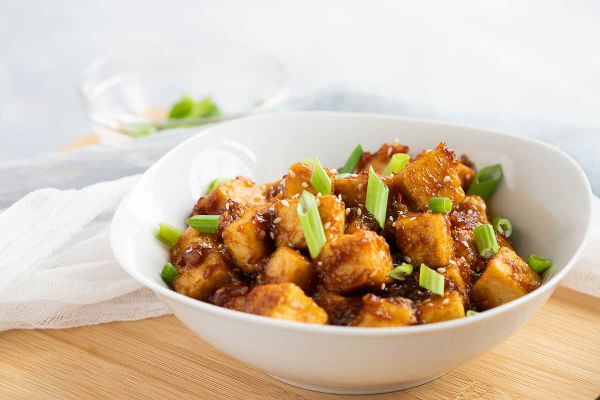 Teriyaki tofu cubes in white bowl topped with scallions.