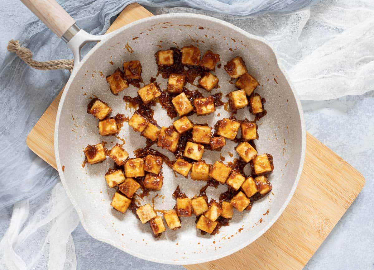 Crispy pan-fried tofu cubes coated in teriyaki sauce in skillet.
