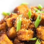 Crispy pan-fried tofu cubes in bowl topped with scallions.