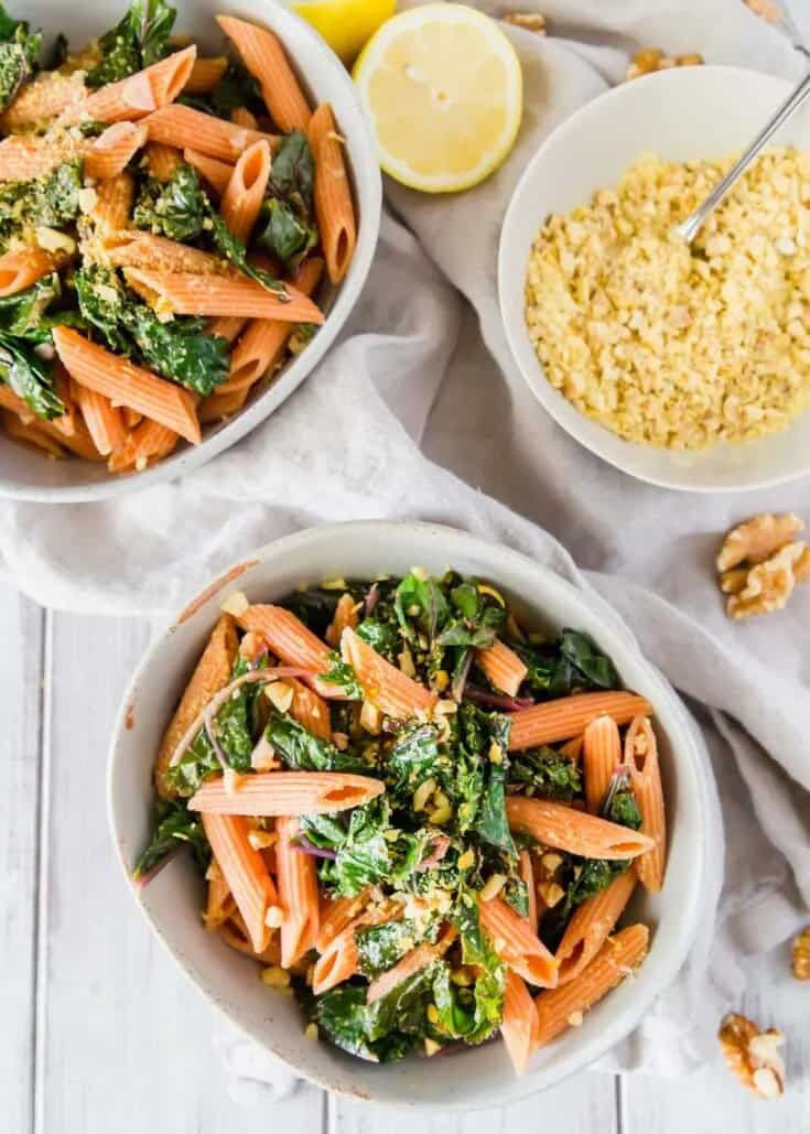 Red lentil pasta with greens and vegan parmesan in white bowls.