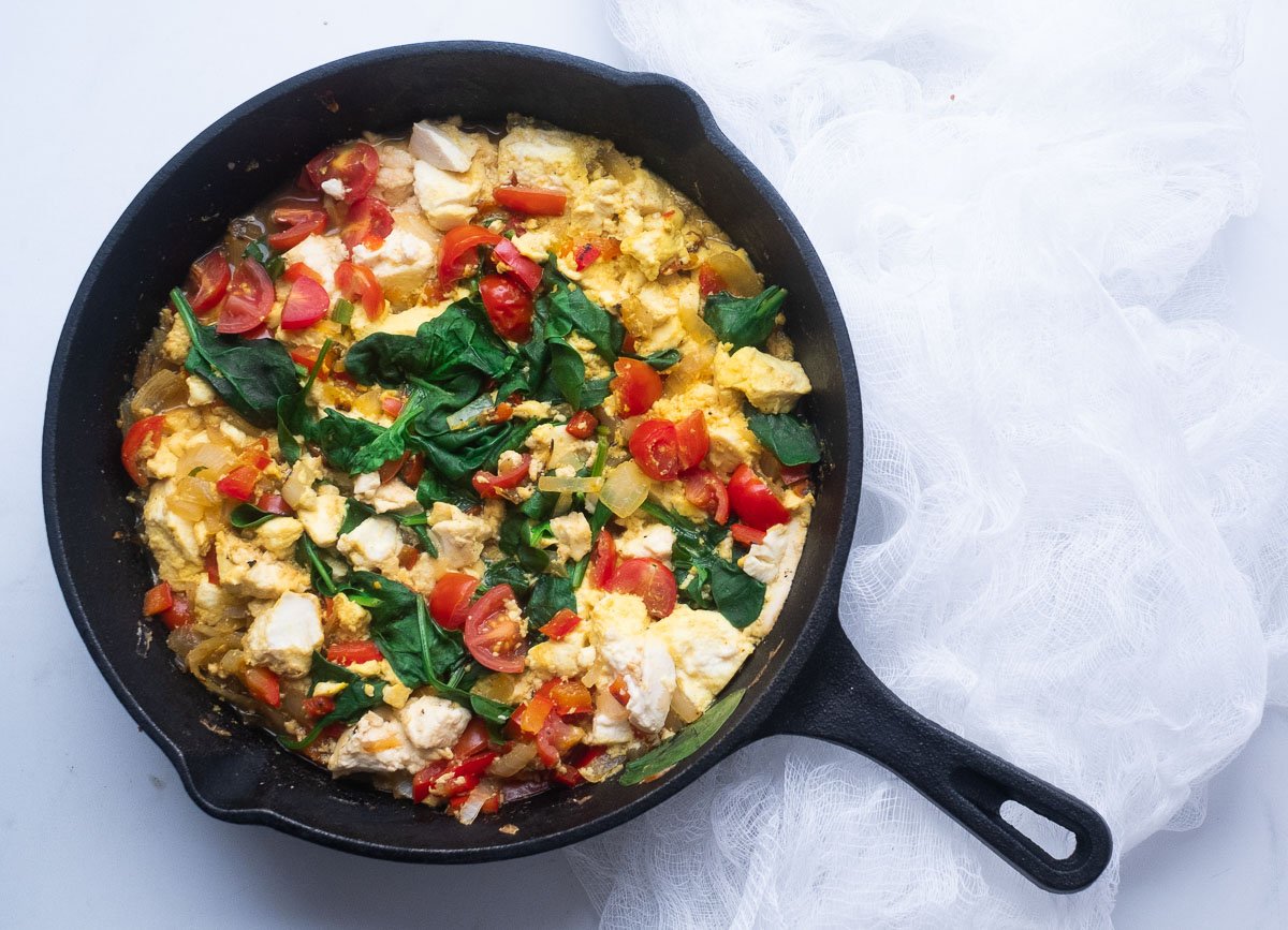 Silken tofu scramble with spinach and cherry tomatoes in skillet. 