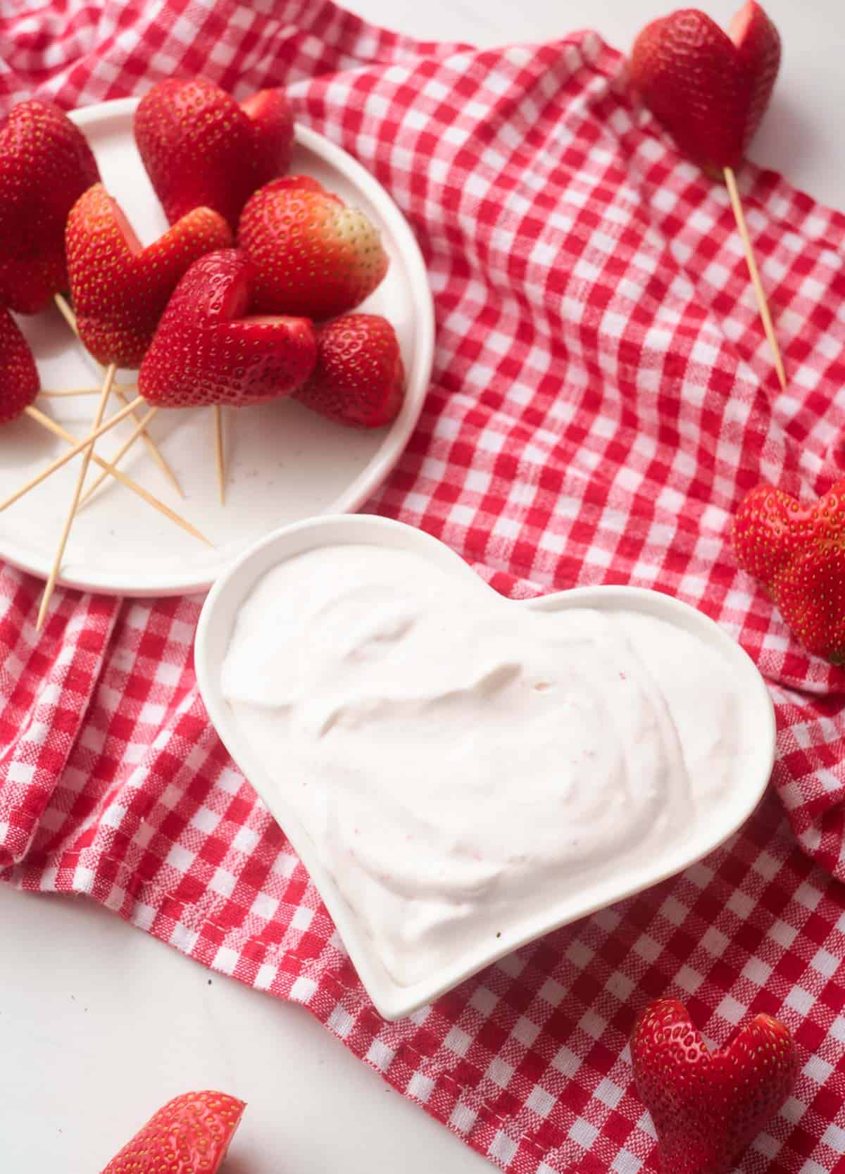 Heart shaped strawberries on toothpicks served with a side of strawberry yogurt in a heart shaped bowl. 