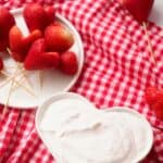 Strawberry hearts on sticks with yogurt dipping sauce in heart shaped bowl.
