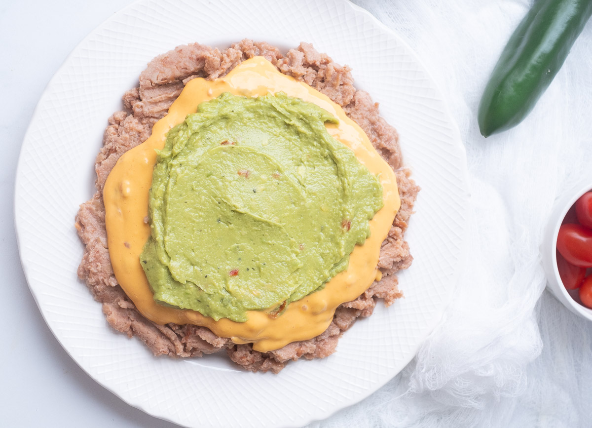 Pinto beans spread on plate, topped with cheese sauce, and guacamole. 