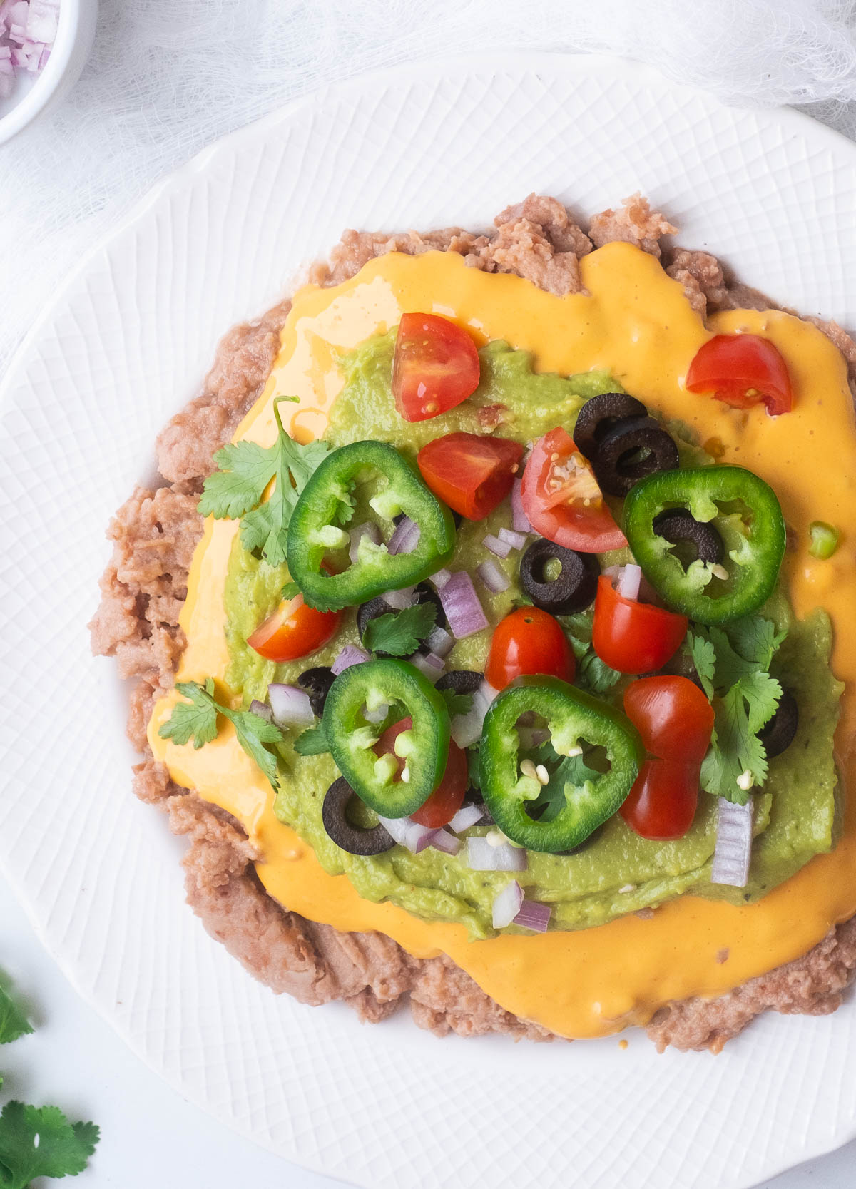 Vegan 7 layer dip with refried beans, cheese sauce, guacamole, and fresh vegetables.