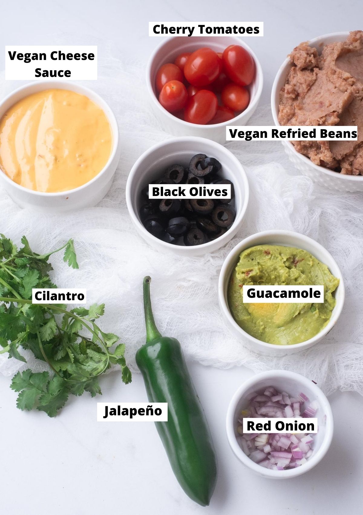Vegan 7 Layer Dip Ingredients: Refried beans, guacamole, vegan cheese sauce, onions, jalapeño, black olives, cherry tomatoes.