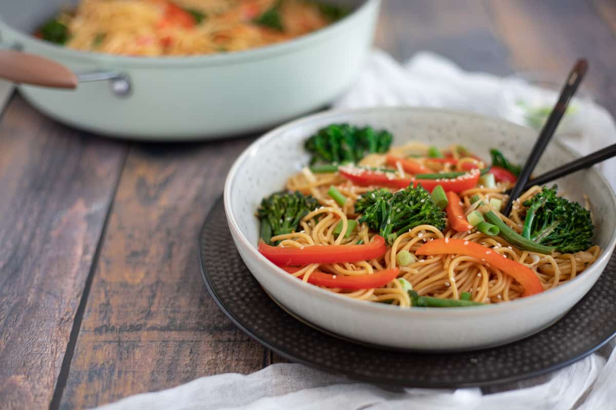 Vegetable chow mein noodles in wide bowl with pot in the background.