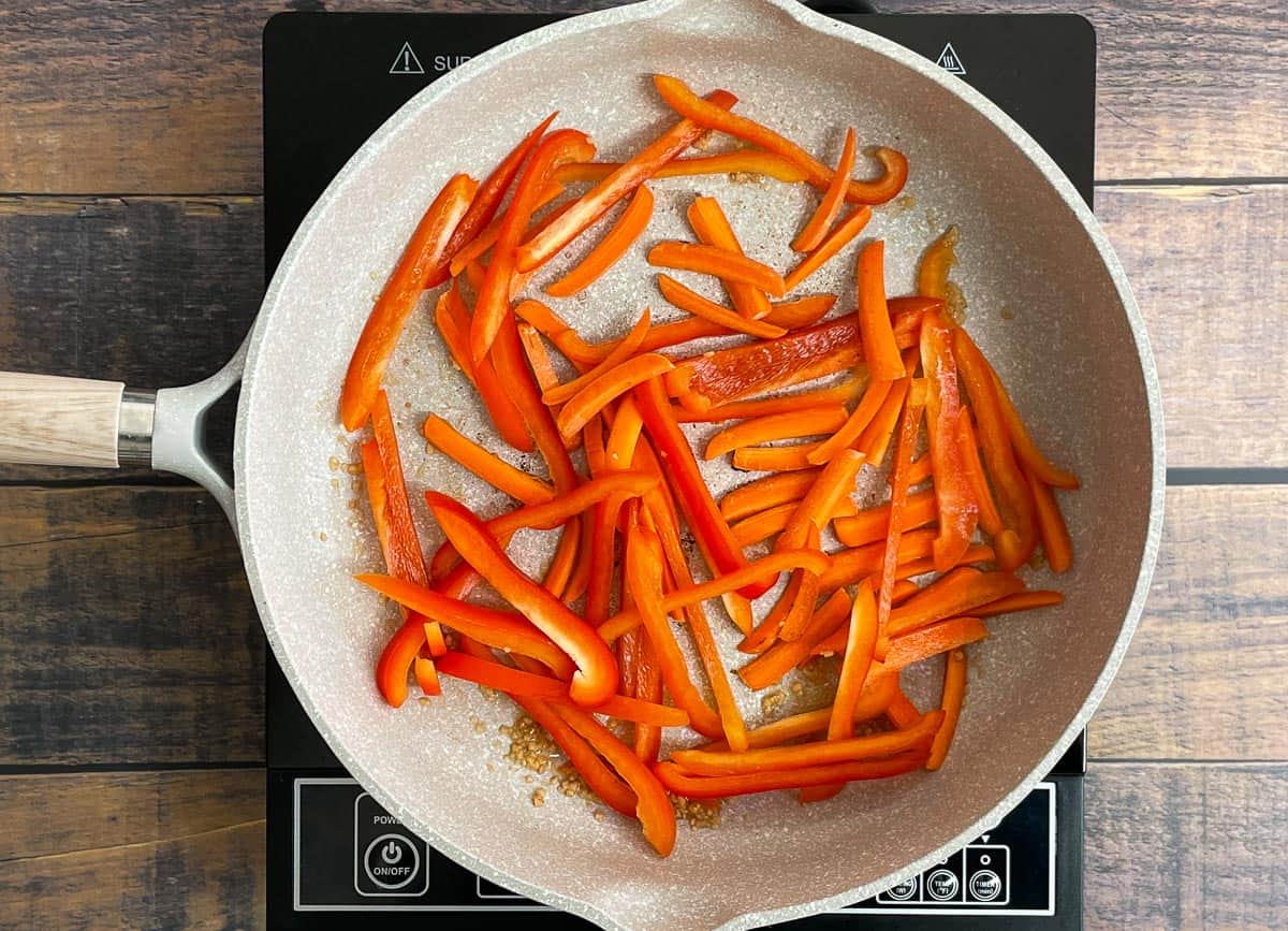 Thinly sliced carrots, and red peppers in sauté pan. 