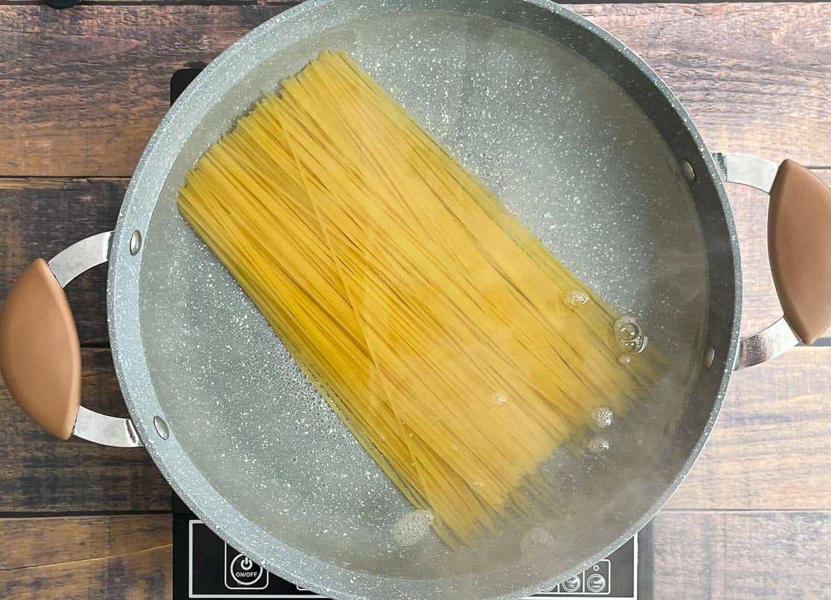Spaghetti noodles added to pot of boiling water.